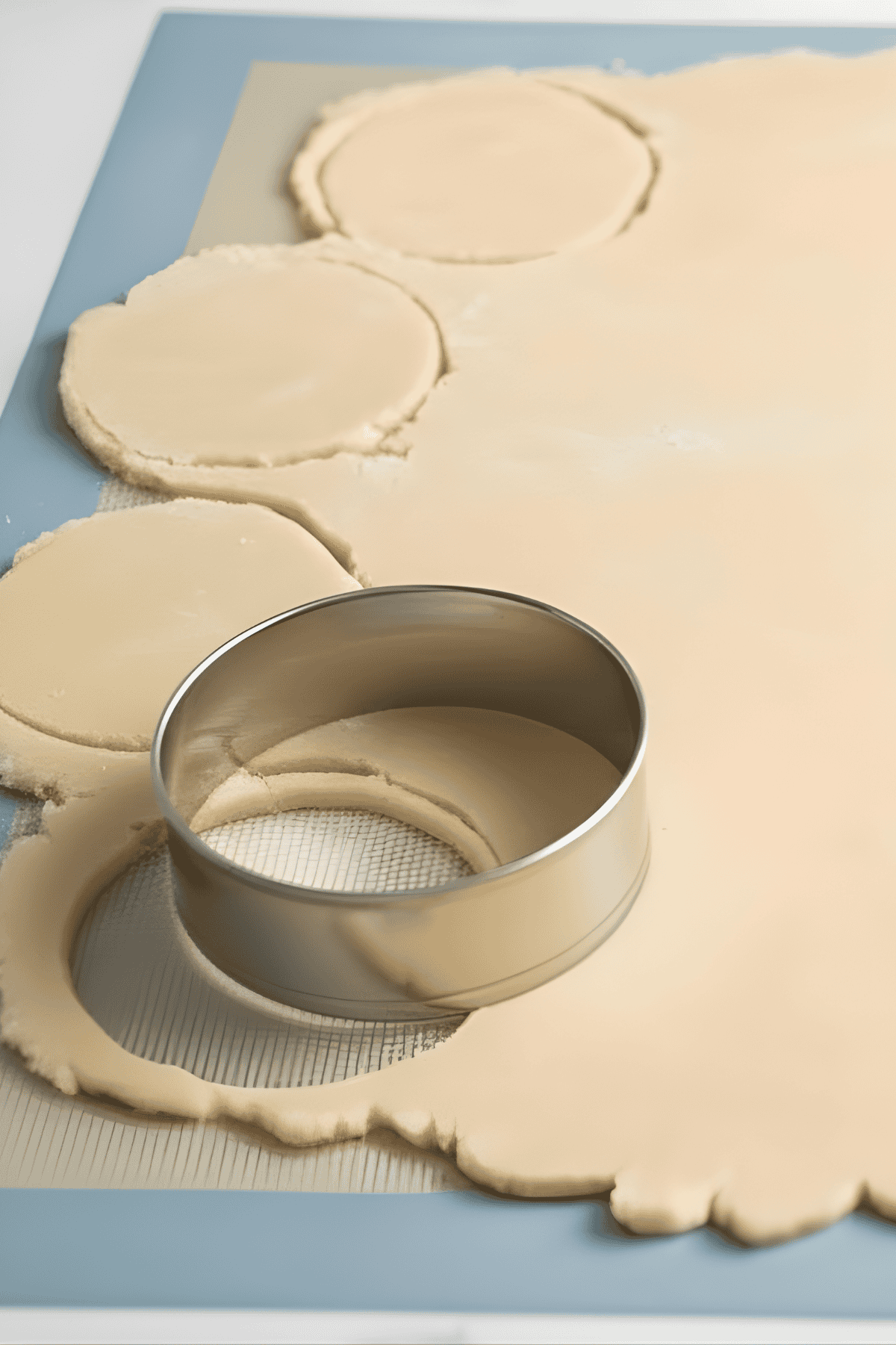 Butter cookie dough rolled out with cookie cutter on silicone baking mat.