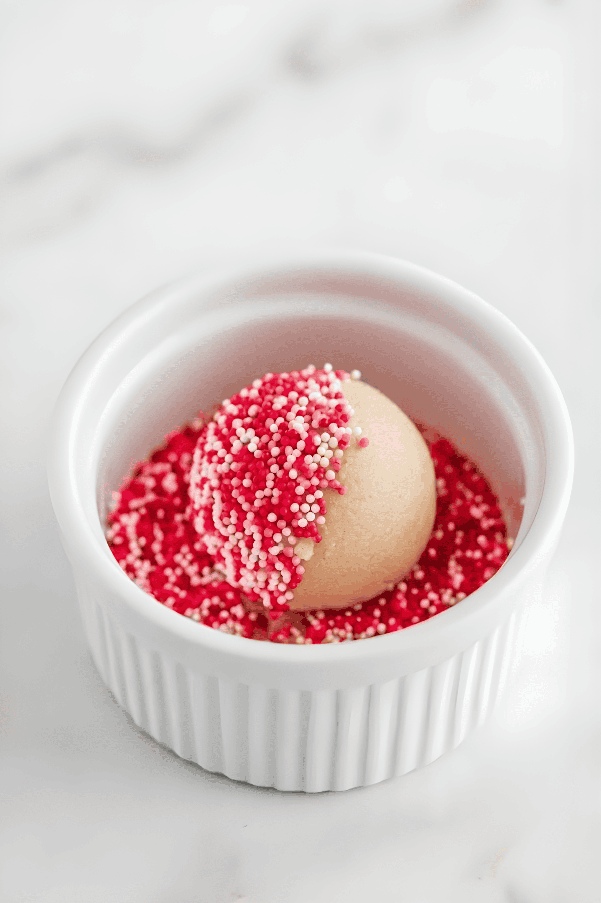 Delicious vanilla ice cream topped with colorful pink and white sprinkles in a white ramekin.