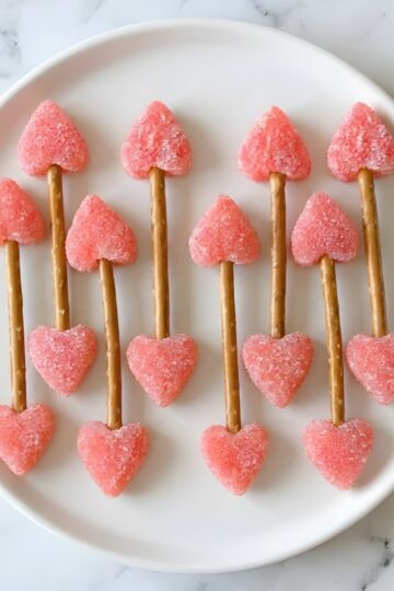 Delicious pink sugar-coated heart-shaped cookie pops on pretzel sticks, perfect for Valentine's Day treats.