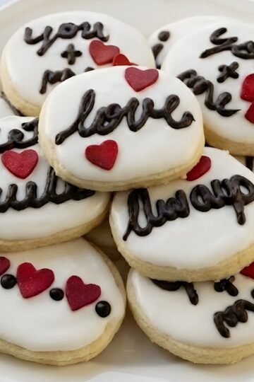 Sweet Valentine cookies decorated with white icing, red hearts, and "love" script in chocolate, perfect for romantic celebrations.
