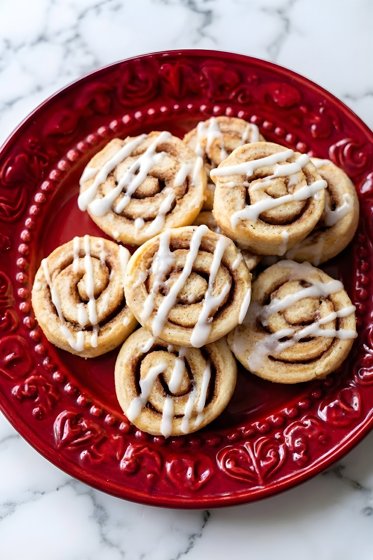 Delicious homemade cinnamon roll cookies drizzled with white icing on a red decorative plate. Perfect for cookie lovers.